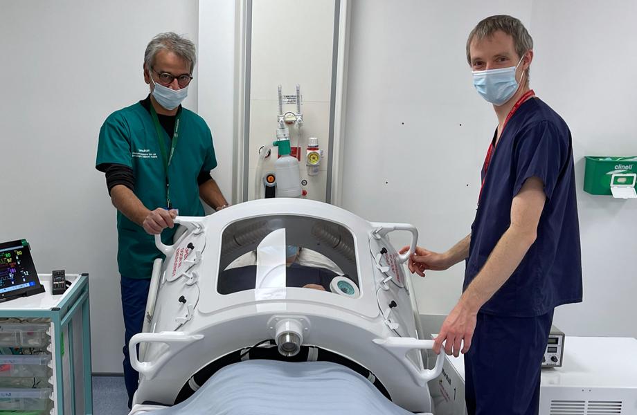 Two medical staff lifting the top off the patient enclosure for the Exovent negative pressure ventilator