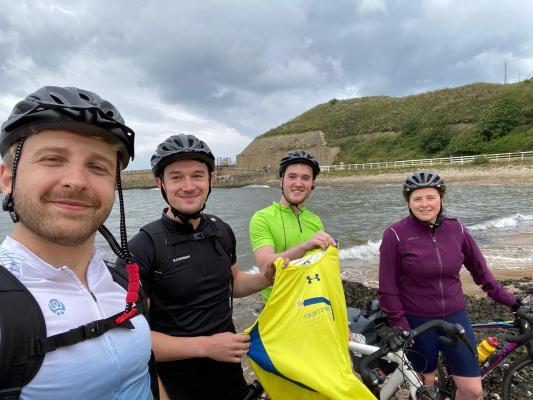 From left to right Dan Potts, Alex Hagan, Jake Kennedy, and Sarah Pagan on their charity bike ride in front of the sea and hills.