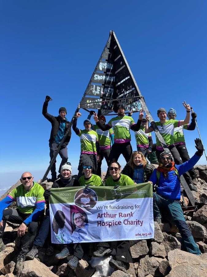 Group of men and women dressed in green at the top of a mountain with a sign 