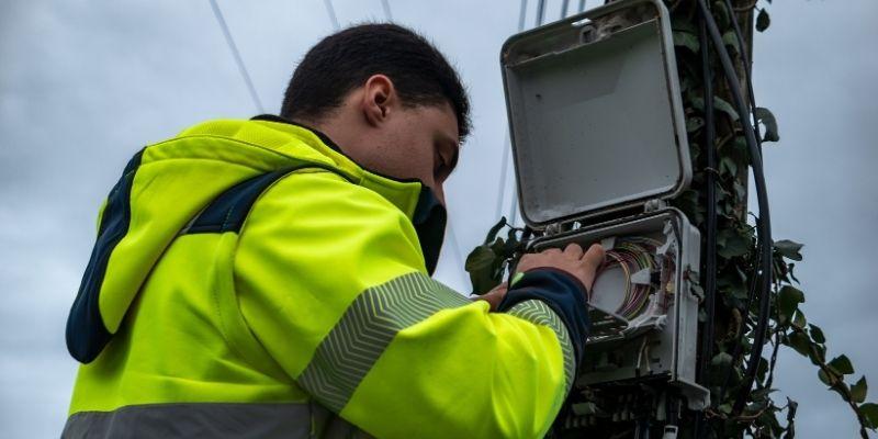 Telecom field engineer in a high-visibility jacket working on a box with cables in it