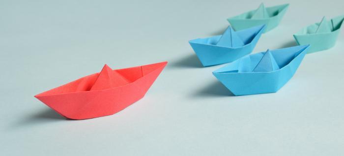 red paper boat leading two blue paper boats
