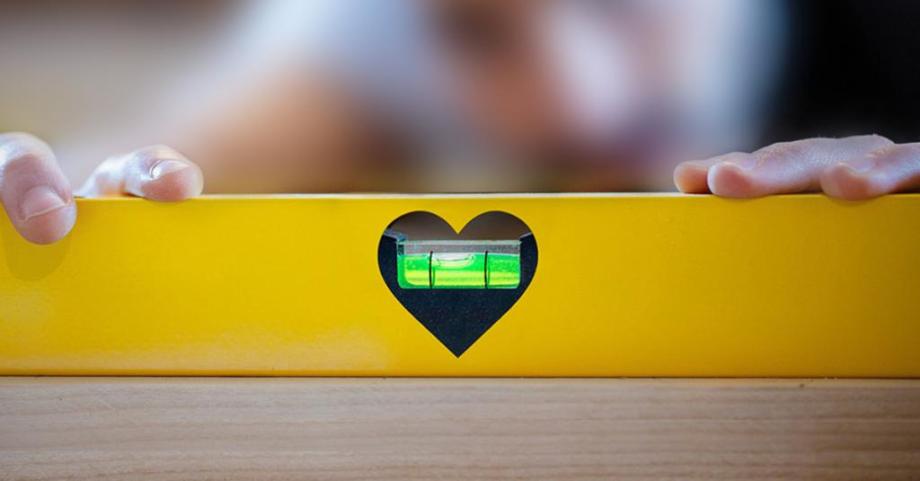 Hands hold a spirit level, in which the viewing window is in the shape of a heart