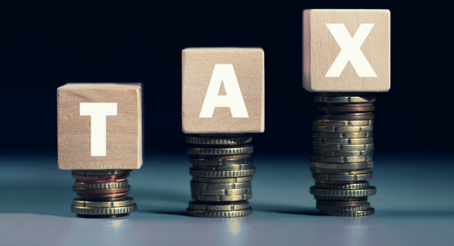 Letter blocks spelling out TAX balancing on stacks of coins