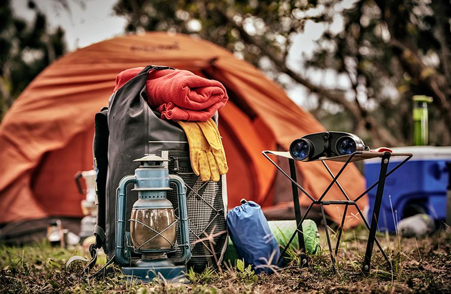 An orange tent with a rucksack in front with a blanket, gloves and oil lamp