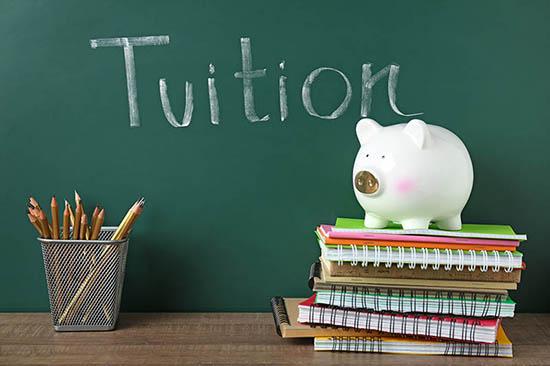 piggy bank and school books beside blackboard saying 'tuition'