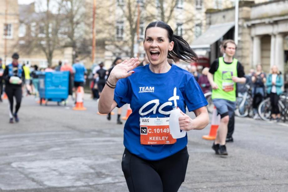 Woman waving while running the Cambridge Half Marathon in ACT t-shirt