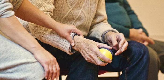 elderly person's hands being held, in one of which is a ball