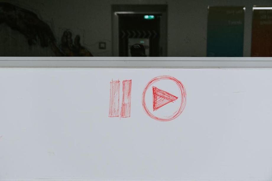 White board with drawn on play and pause button in red pen.