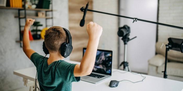 Child watching laptop and wearing headphones holds his arms above his head