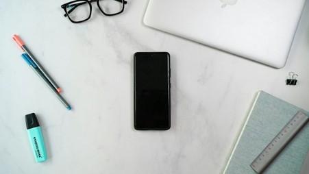  A phone, laptop and notebook on a desk. 